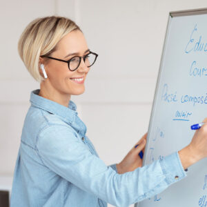 Female teacher with glasses writing French on a whiteboard during a lecture.
