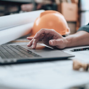 A person diligently working on a laptop, reviewing construction plans.
