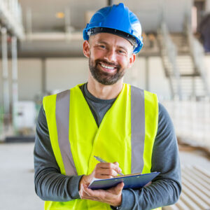 Construction worker with clipboard, wearing hard hat and safety vest.