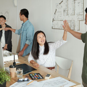 A group of people in an office celebrating success with other person enthusiastically giving a high five.