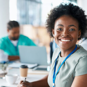 A woman sits among a group of individuals at a table, and smiling at camera.
