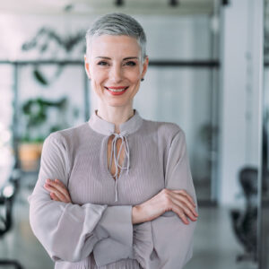 A mature woman with gray hair standing in an office, surrounded by desks and office equipment.