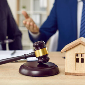 A judge gavel and a wooden house on a desk symbolize legal issues in housing, representing the intersection of law and real estate.