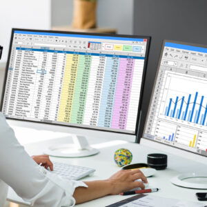 A person working with a computer on excel sheets with two screens.