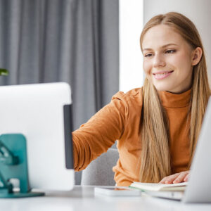 A woman smiling while using a laptop and a tablet to work on her tasks.