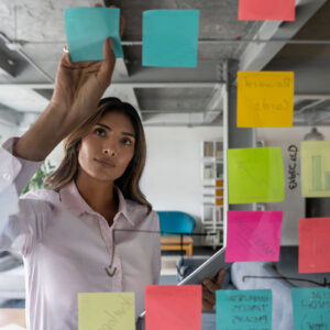 A person writing on a glass wall with sticky notes.