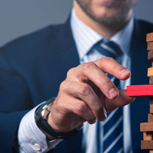 A man in a suit holds a wooden block, carefully arranging a stack of wooden block.