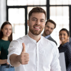 A group of people behind a man who is giving a thumbs up.