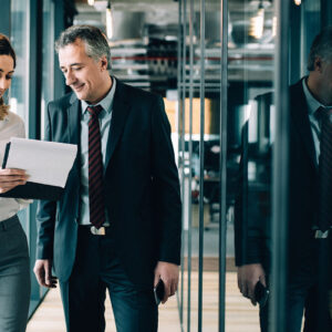 Two professionals in office hallway, discussing work.