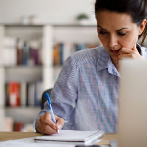 A woman sitting at a desk with a pen and notebook, preparing for an exam.