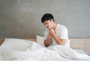 Young man in bed feeling his neck, looking like he has a sore throat
