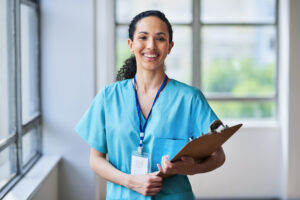Smiling medical professional in scrubs holding a clipboard in a hospital setting