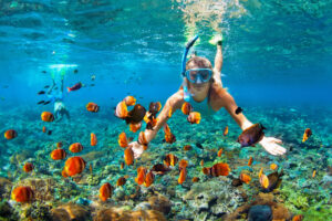 Young woman underwater in snorkeling mask, with tropical fish in coral reef sea pool